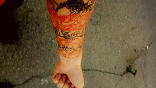 Close-up of a detailed black and red tattoo on forearm in a minimalist studio setting.