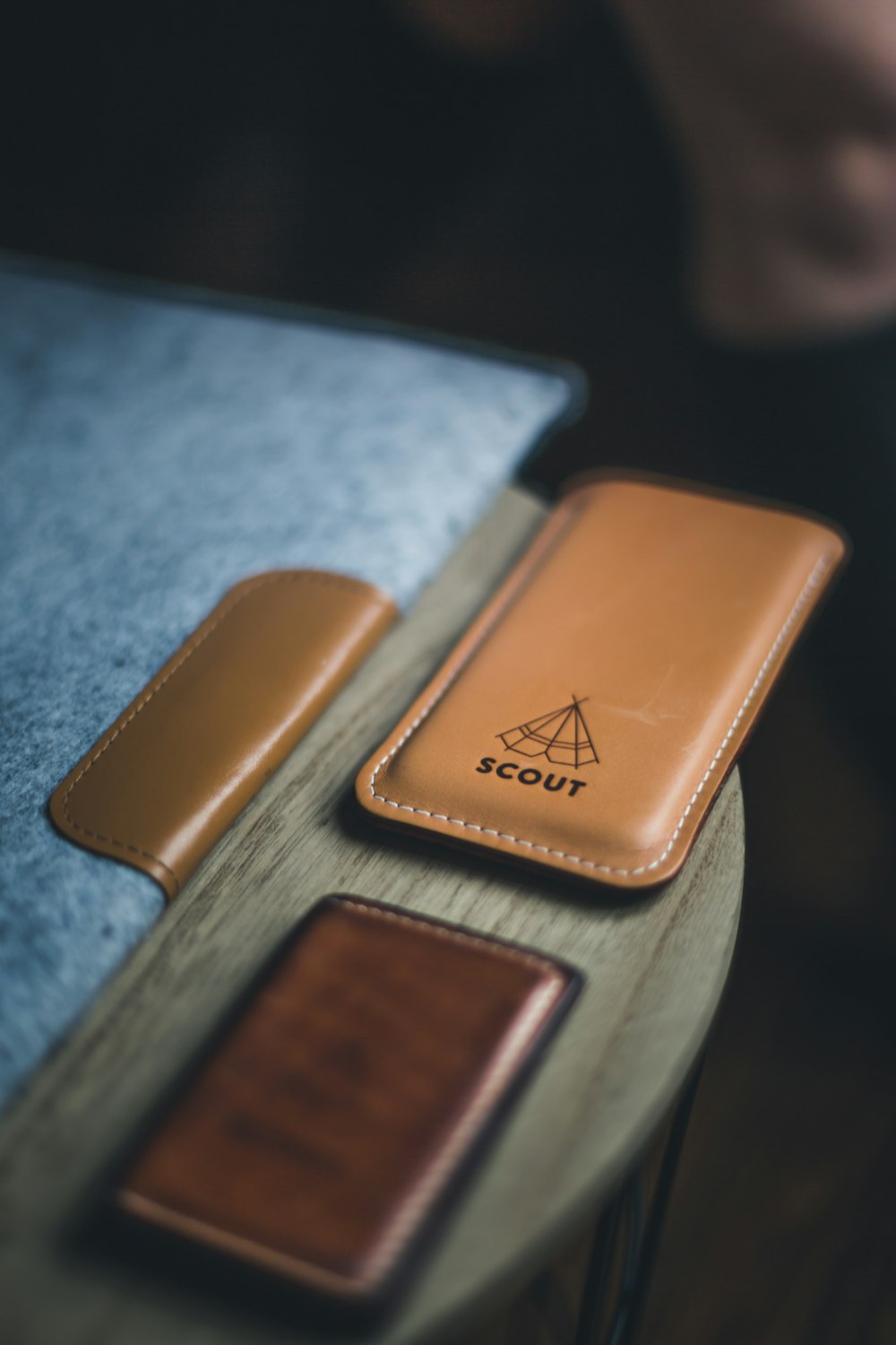 Housse d’ordinateur portable, portefeuille et support de téléphone en cuir avec une étiquette indiquant « SCOUT » sur une table circulaire en bois