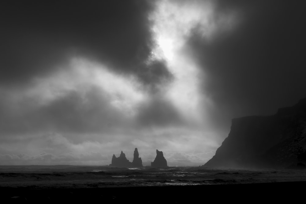 grayscale photo of rock formation surrounded by water