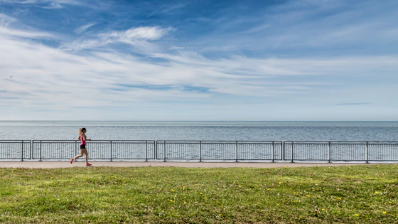 Mulher correndo em um calçadão à beira do mar, vista de costas, com tênis vermelhos, em foto diurna
