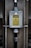 A warning sign with the text 'CUIDADO RISCO DE CHOQUE ELETRICO MANTENHA DISTANCIA DE SEGURANCA SUPERIOR A 3 METROS' in a yellow triangle, indicating an electrical shock hazard. The sign is mounted on a gray box fixed to a stone wall, with black pipes connected to the box.