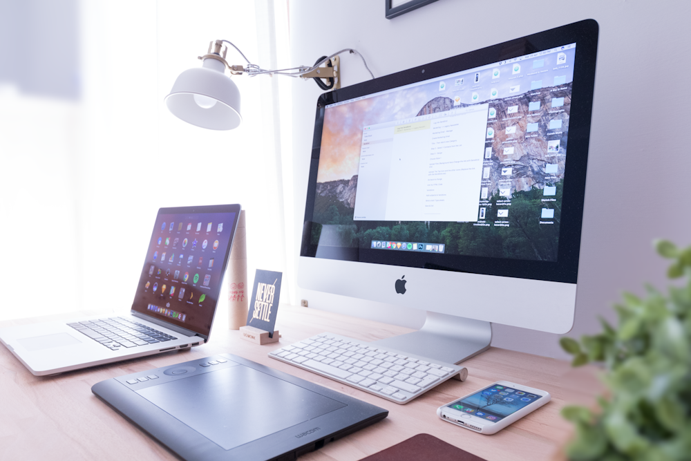 A busy workspace with a MacBook, an iMac, an iPhone and a drawing tablet