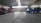 A large indoor garage or depot with a high, steel-beamed ceiling. The space contains multiple vehicles, including a red truck, a yellow armored van, and a blue bus. The vehicles seem to be parked or possibly undergoing maintenance.