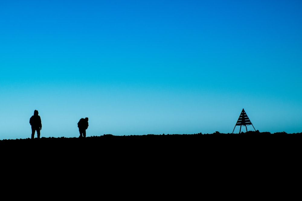 Silhouette von zwei Personen, die tagsüber in der Nähe eines Zeltes auf dem Boden stehen