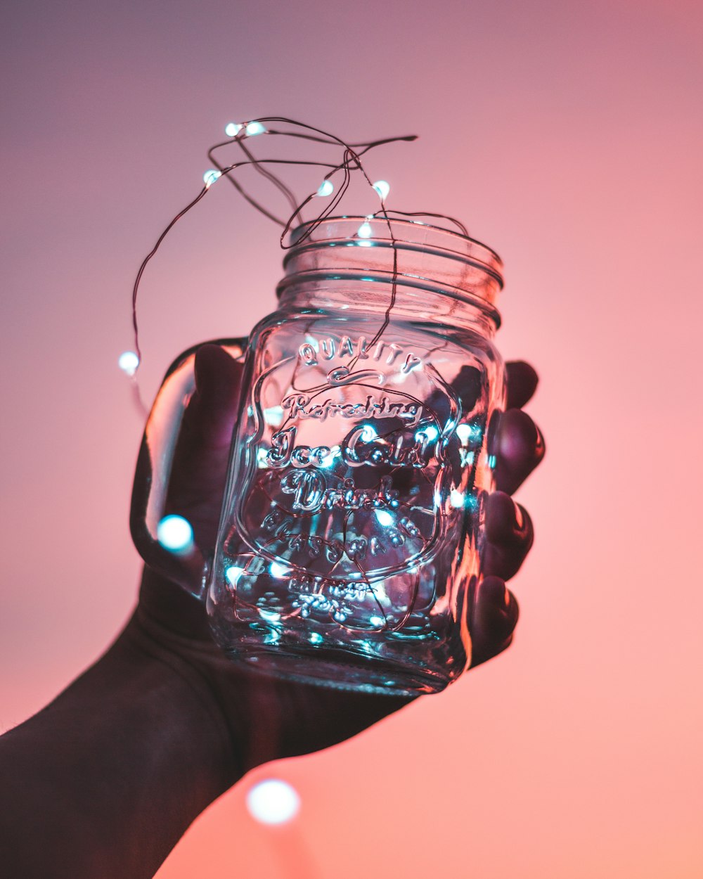 persona sosteniendo un frasco de vidrio transparente con tiras de luces en el interior
