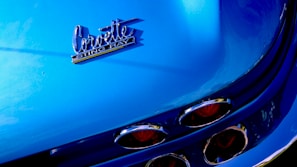 The image features a close-up of a blue Corvette Stingray, highlighting the car's rear emblem and distinct tail lights with chrome details.