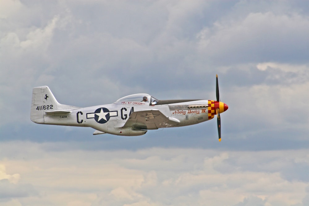 silver propeller jet fighter above white clouds