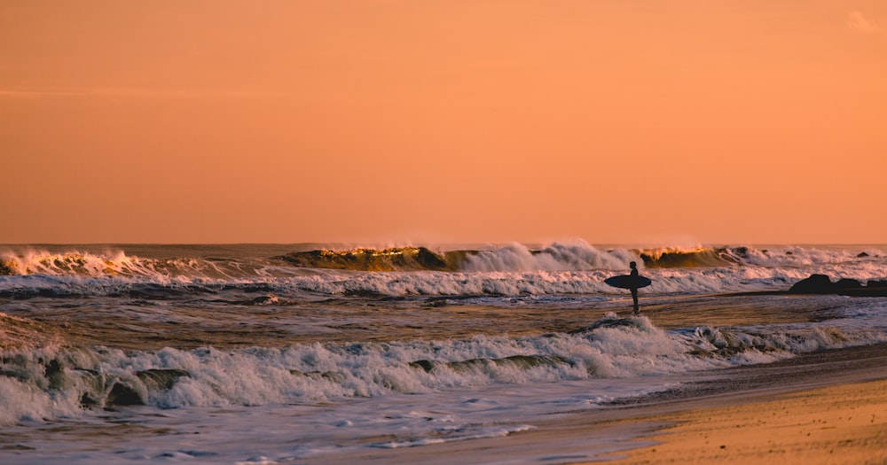 Surfer standing in shallow water, looking at waves at sunset in Bradley Beach