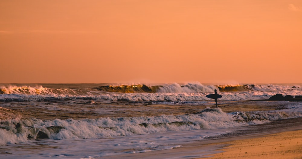 Surfista de pie en aguas poco profundas, mirando las olas al atardecer en Bradley Beach