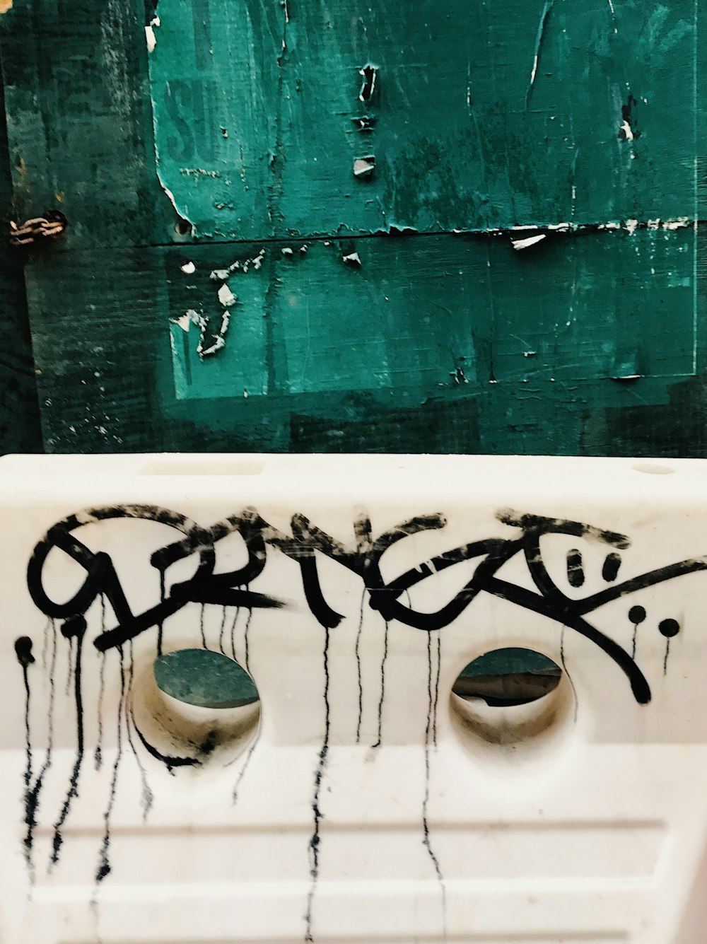a white sink with graffiti on it in front of a green wall