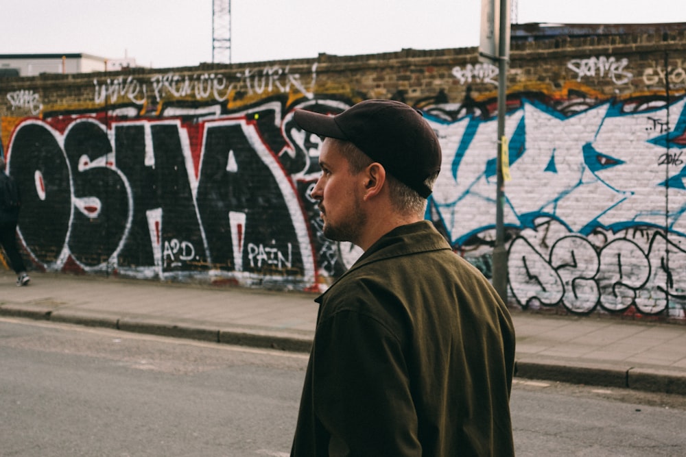 man walking on asphalt road near wall with graffitis