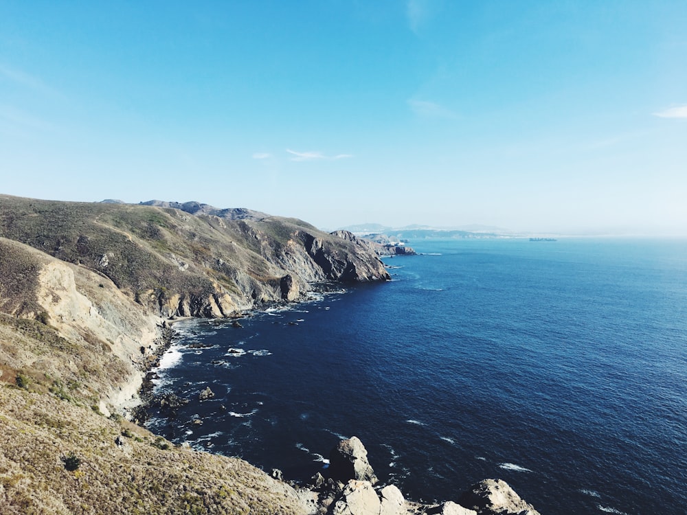 cliff beside ocean under clear blue sky during daytime