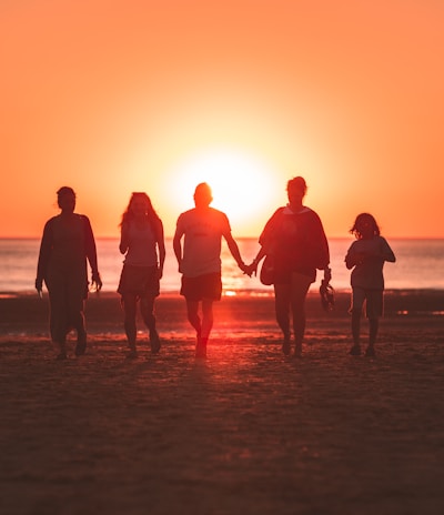 silhouette photo of five person walking on seashore during golden hour