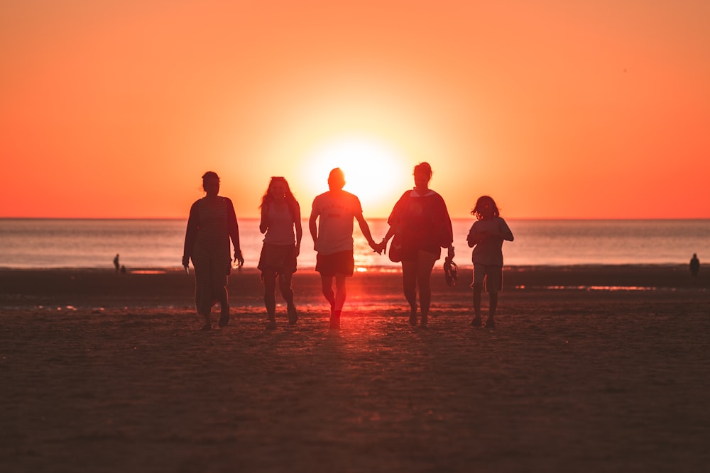 silhouette photo of five person walking on seashore during golden hour