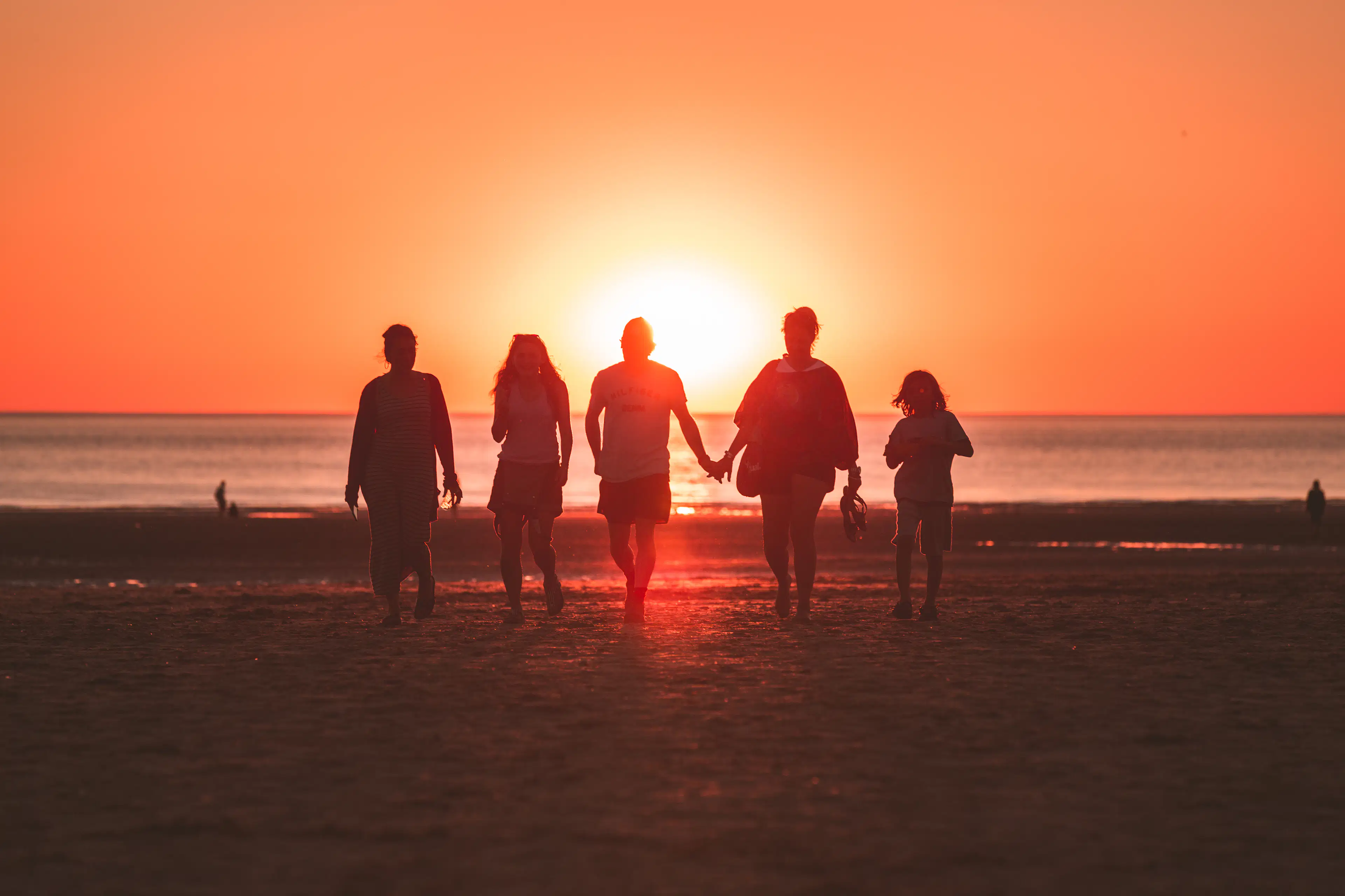 Travellers walking together in silhouette along a shore at golden hour, warm sunset light behind them