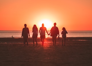 silhouette photo of five person walking on seashore during golden hour