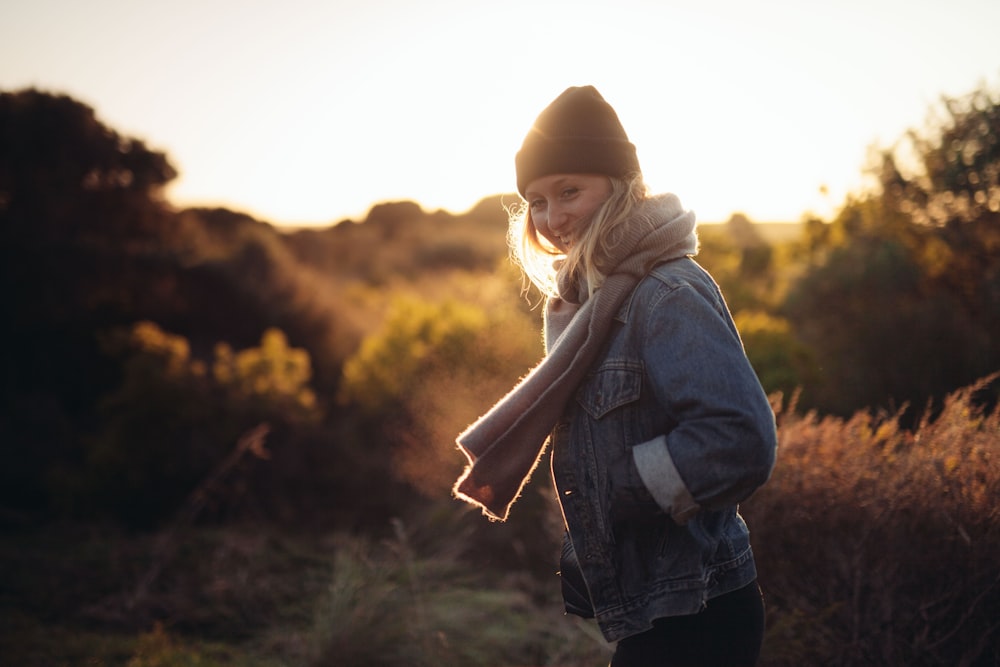 smiling woman taking photo near trees and brown grass during sunrise
