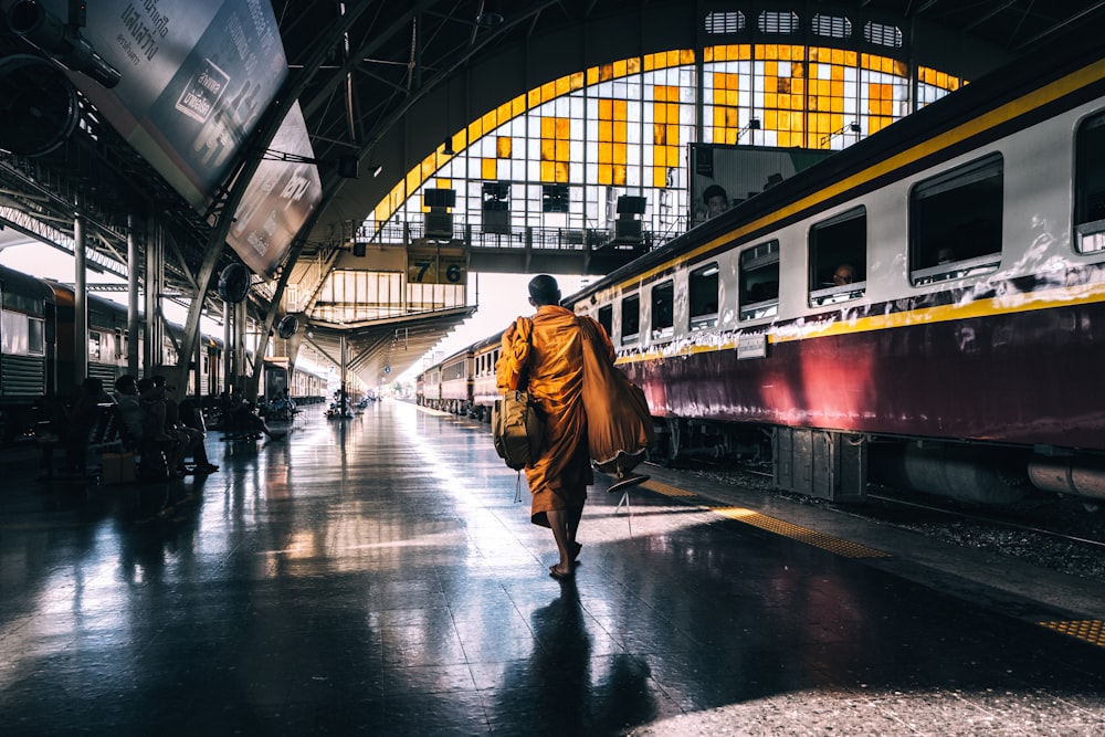 A monk in orange robes walking across a railway platform in Bangkok