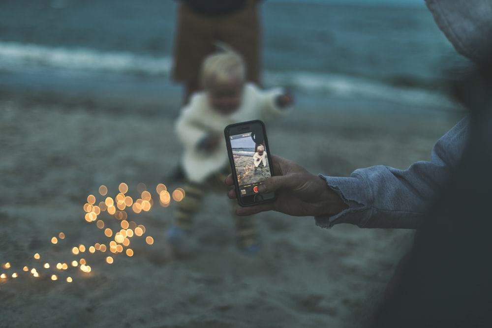 person using smartphone capturing baby on brown sand