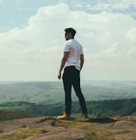 man standing on bolder overlooking the hills and mountains