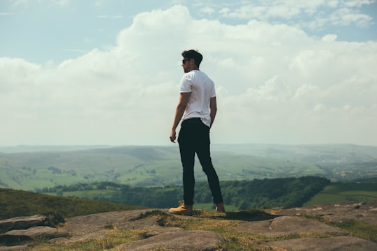 man standing on bolder overlooking the hills and mountains in Stanage Edge United Kingdom