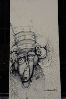 A monochromatic drawing of an abstract face with exaggerated features, including large eyes and a long nose. The head is adorned with circular elements resembling a whimsical hat or hair. The background is speckled with small dots, creating a textured effect. The artwork includes scripted text and signature at the bottom.