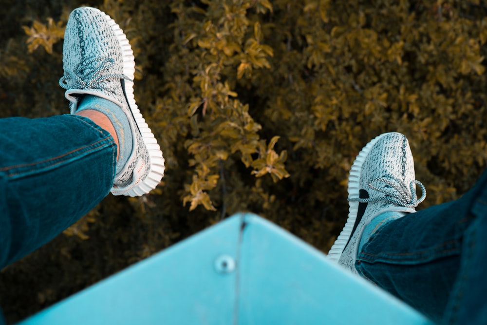 person wearing white adidas sneakers sitting on blue steel frame