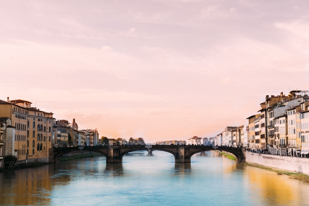 bridge crossing river in town under cloudy sky during daytime