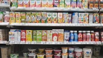 A variety of packaged drinks and yogurt products are neatly organized on grocery store shelves. The top shelf features an assortment of colorful fruit juice cartons, while the middle shelf contains more juice cartons as well as bottled drinks. The bottom shelf displays a selection of yogurt cups and beverages.
