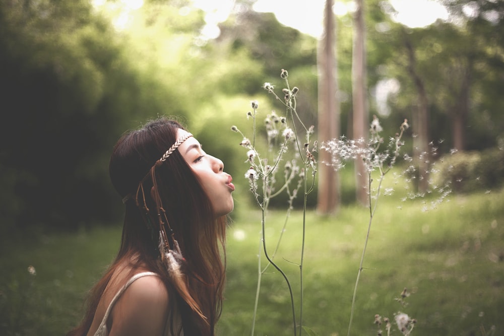 Foto einer Frau, die Löwenzahnblüten bläst