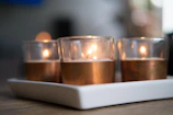 A set of three candles in beige, white, and terra cotta hues arranged on a stone surface.