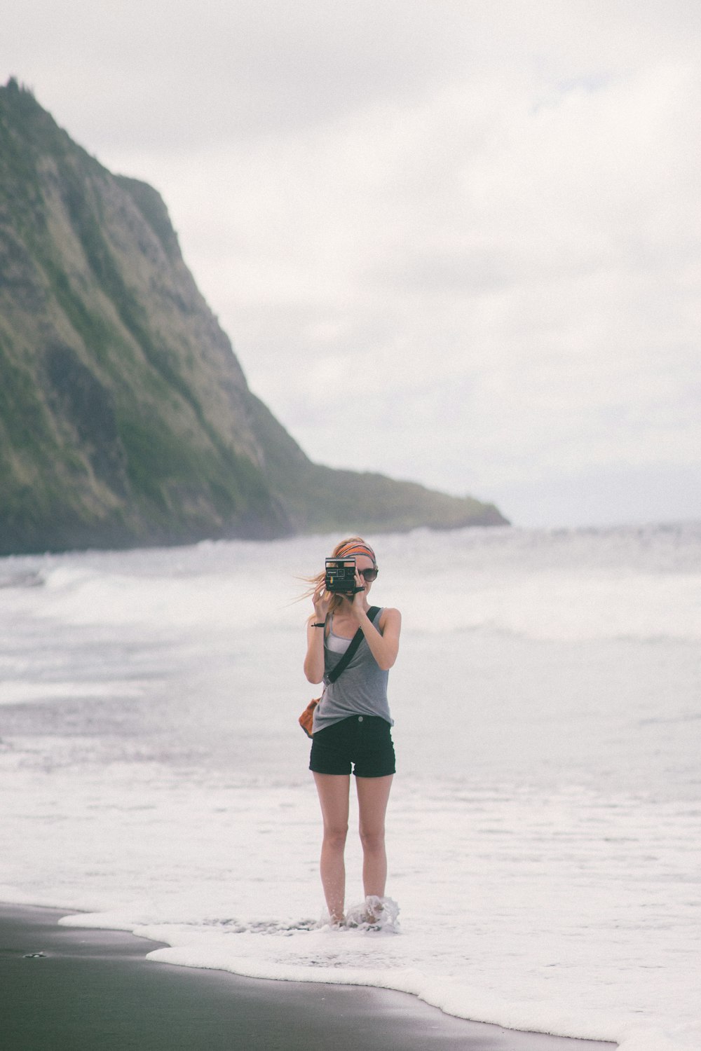 Frau mit Kamera steht am Strand
