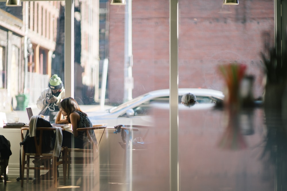 woman sitting on chair near man holding device beside white post at daytime