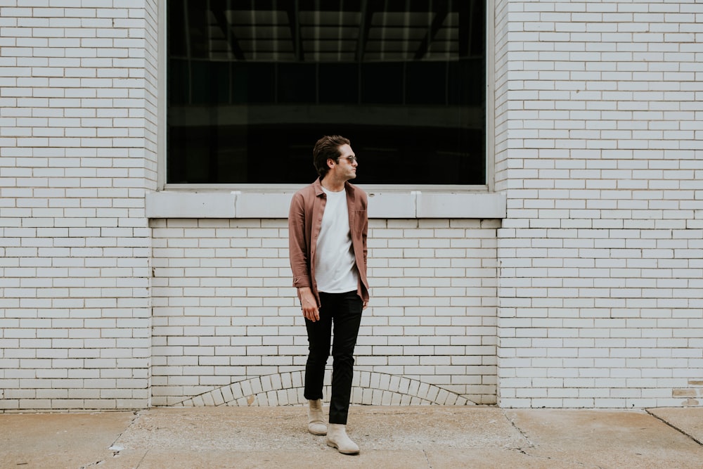 man standing beside beige brick wall