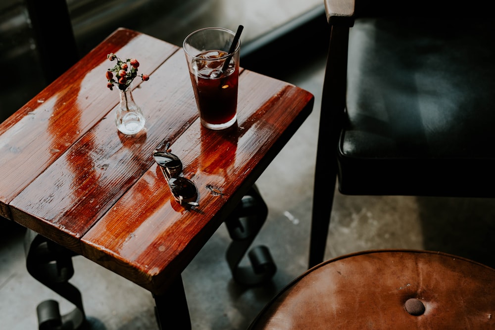 vaso para beber y gafas de sol colocados en una mesa auxiliar cuadrada de color marrón