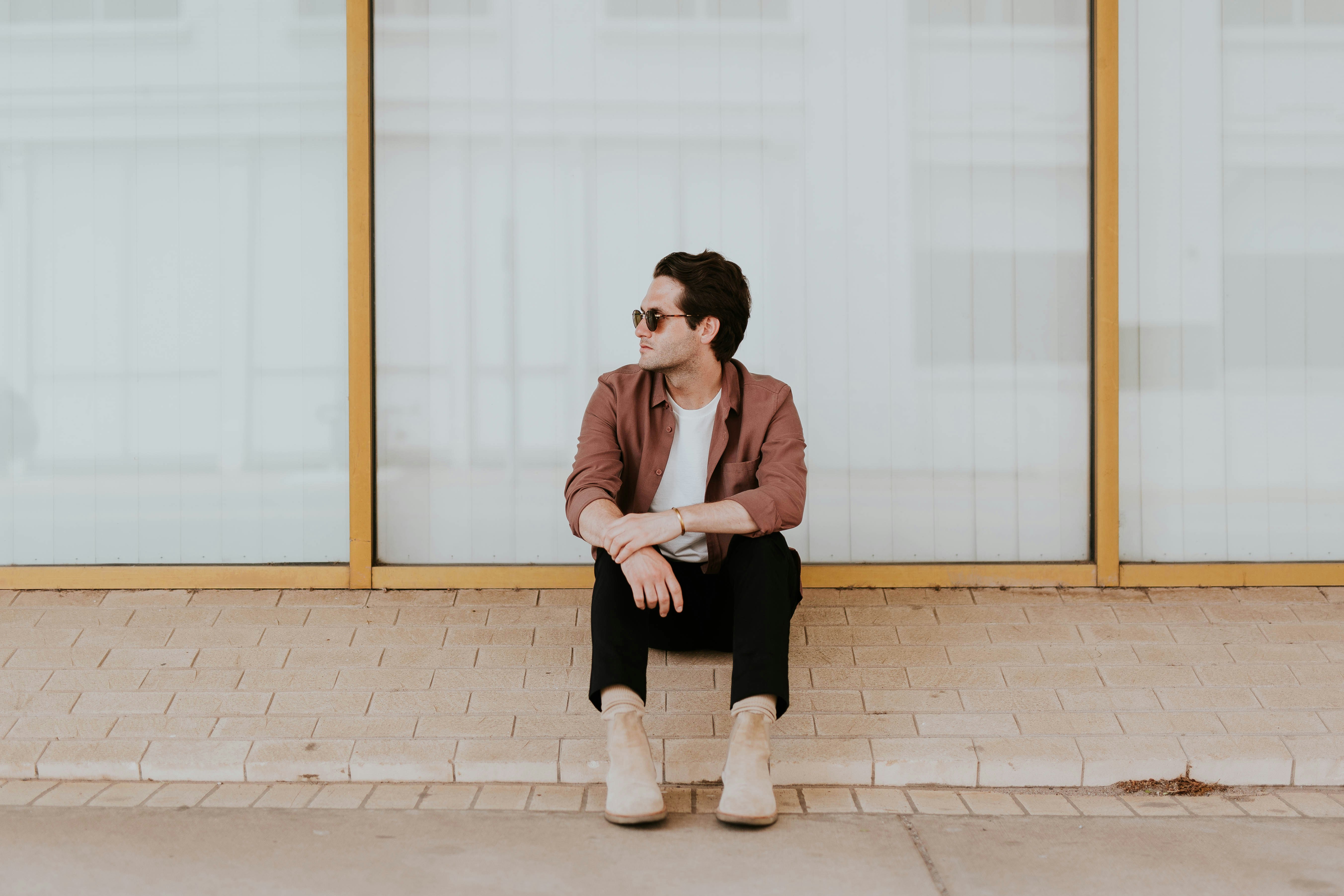 A man in boots sits on a ledge in front of plate glass windows