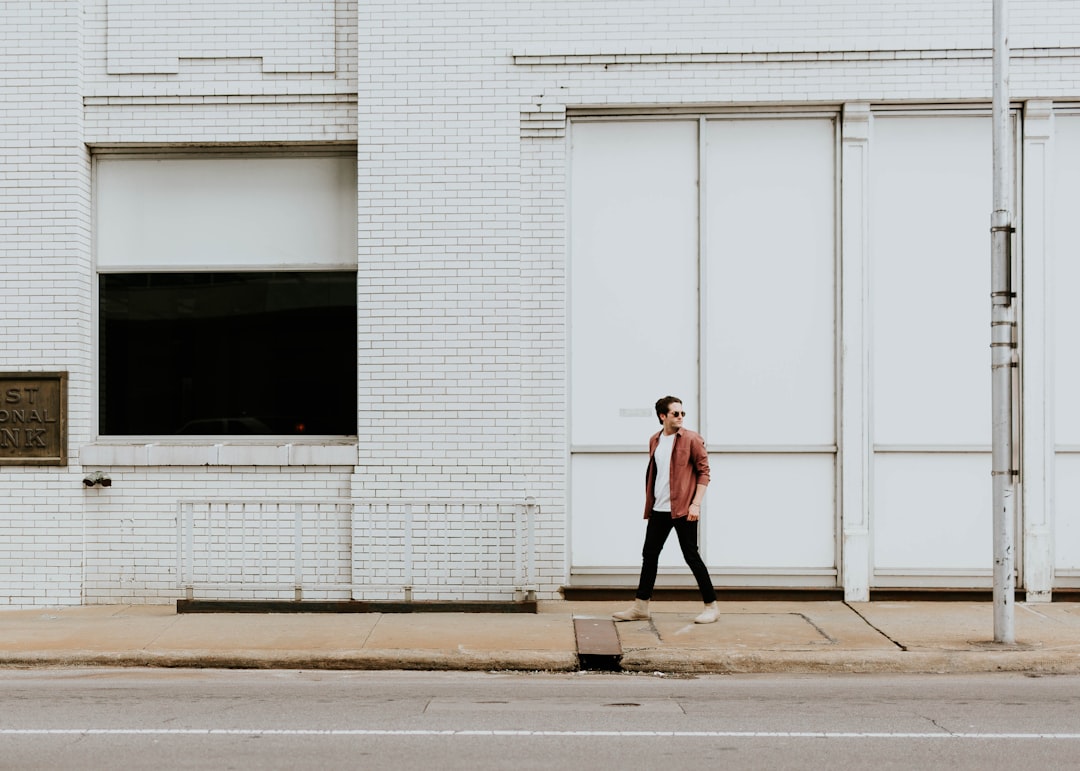 man walking on sidewalk beside white building during daytime