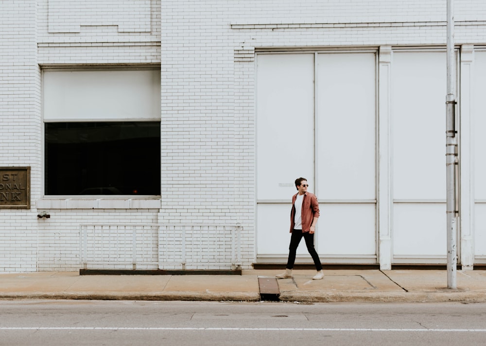 man walking on sidewalk beside white building during daytime