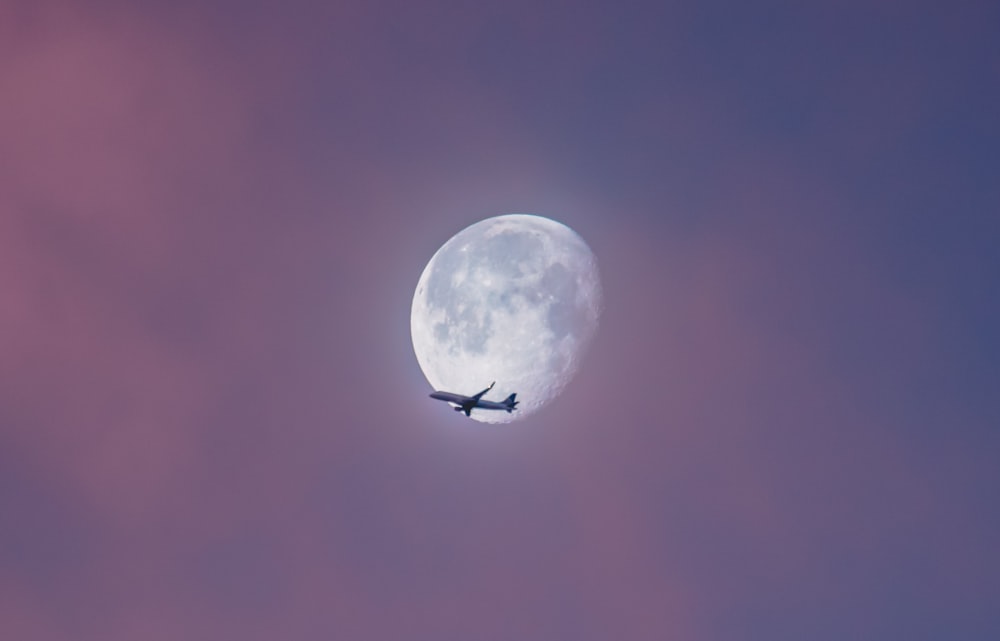 Avión volador en el cielo durante la luna llena durante el día