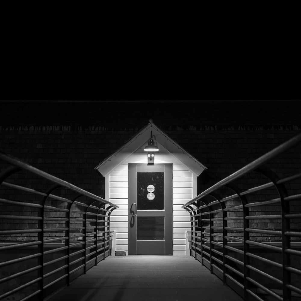 A shed lit up at the end of a bridge during night.