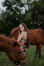 woman standing between brown horses at daytime