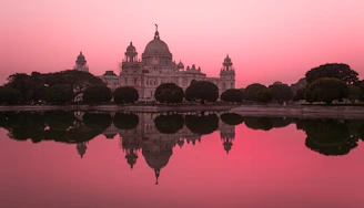 The Victoria Memorial reflected in a calm pond under a pink sky in Kolkata