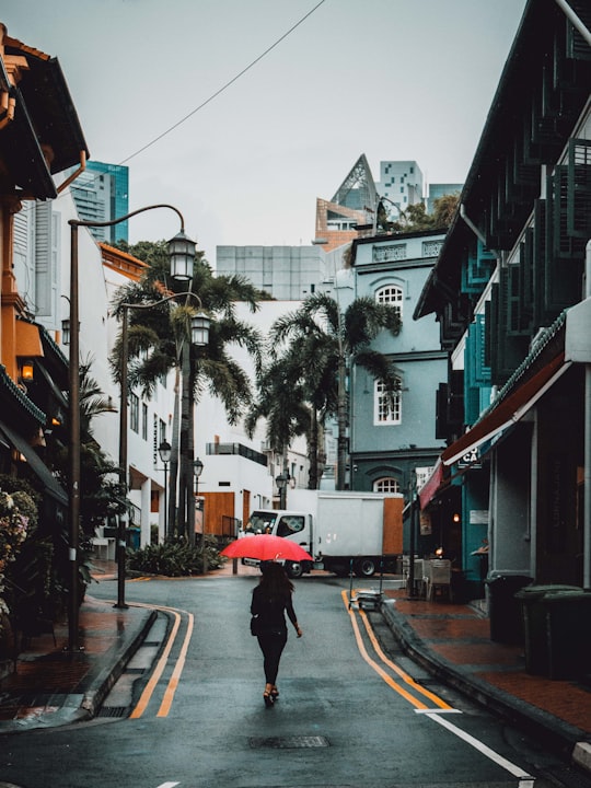 woman holding red umbrella walking on road between buildings at daytime in Chinatown Singapore