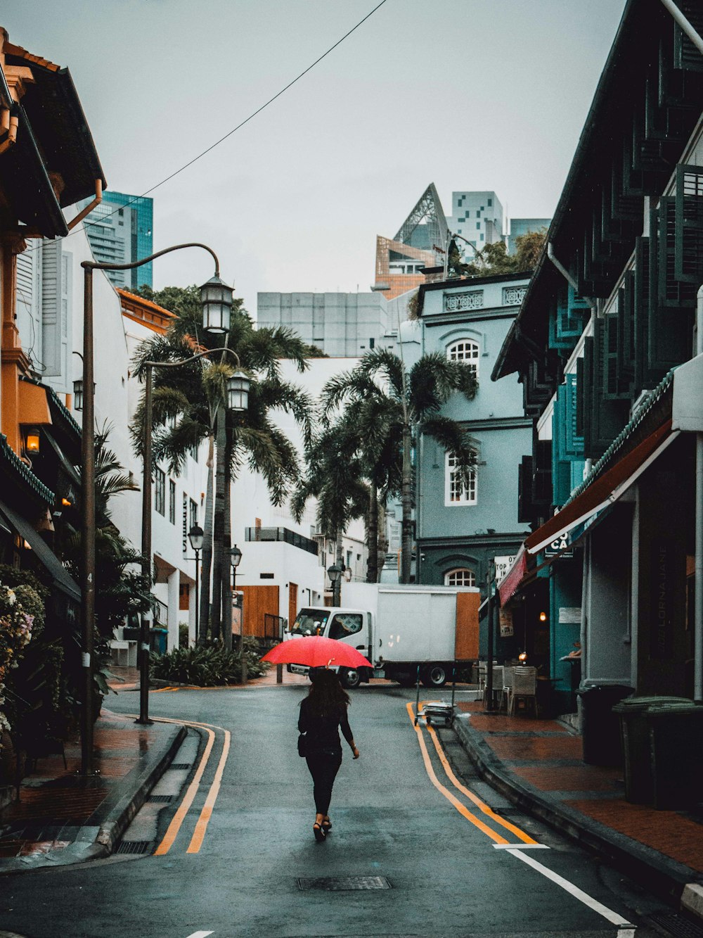 Frau mit rotem Regenschirm geht tagsüber auf der Straße zwischen Gebäuden