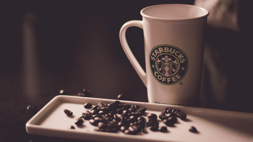 granos de café al lado de la taza de café de Starbucks