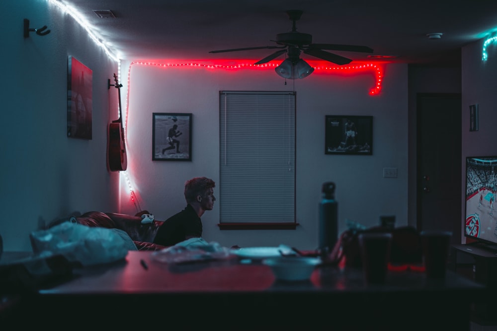 A young man sitting on a leather sofa in a dim room and watching television