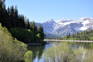 A serene mountain landscape with a calm lake reflecting the sky, surrounded by lush greenery and a few kayakers in the distance.