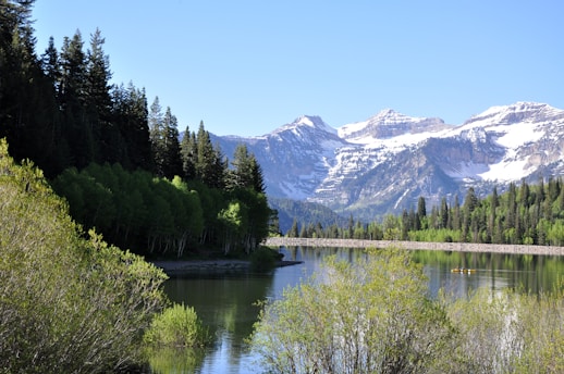 A serene mountain landscape with a calm lake reflecting the sky, surrounded by lush greenery and a few kayakers in the distance.