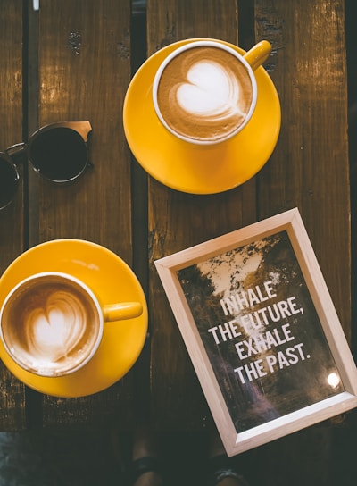 two coffee lattes in yellow cup with saucer on brown wooden table