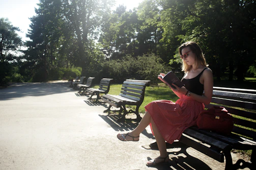 A peaceful outdoor scene with a woman reading a book on a park bench.